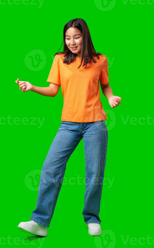 Young woman dancing in an orange shirt and jeans against a vibrant green background photo