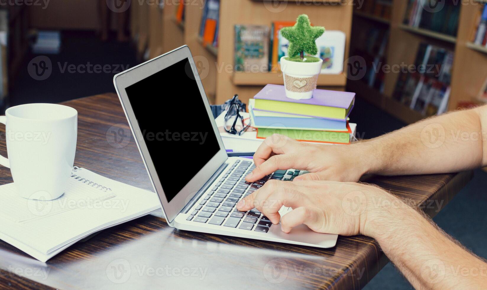 Working on a laptop with books and a coffee cup in a cozy library setting in the afternoon photo