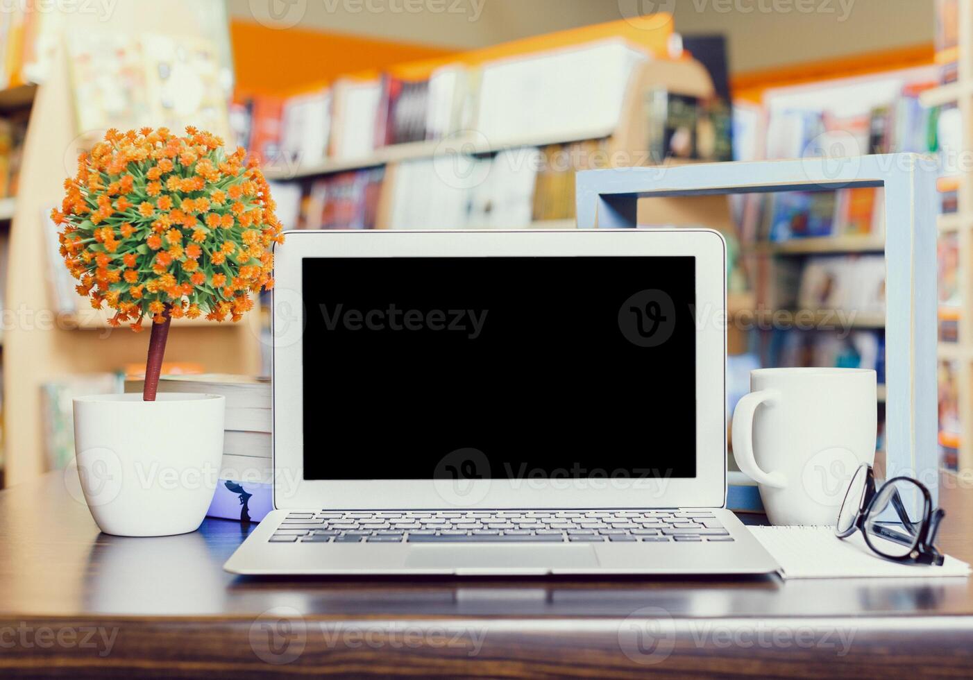Workspace setup with laptop, greenery, and coffee mug in a cozy bookshop environment during the daytime photo