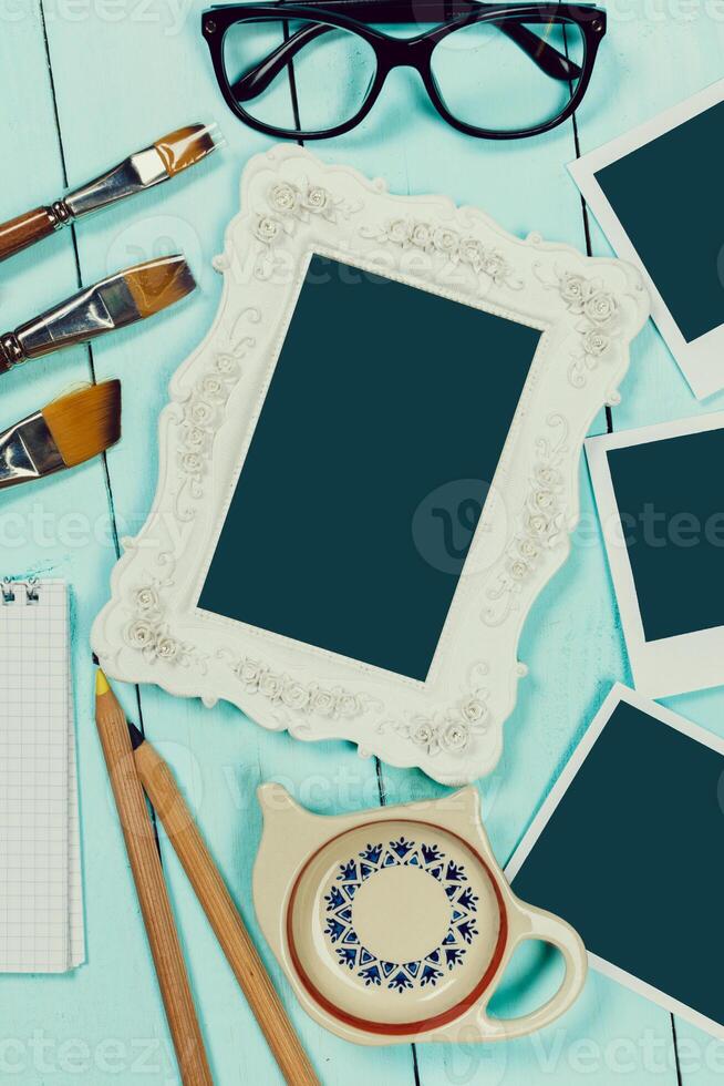 Creative workspace with empty frame, stationery, and coffee cup on turquoise table photo