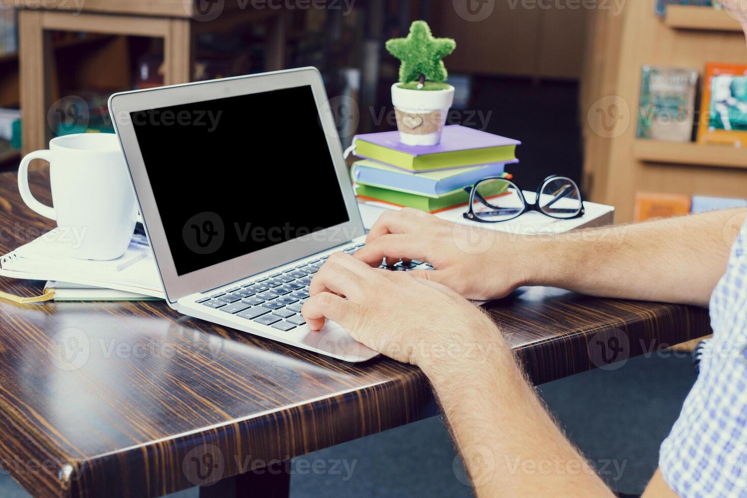 Person working on laptop at a cozy desk surrounded by books and coffee in a quiet indoor space photo