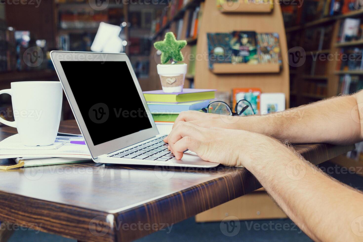 Individual works on laptop at a cozy library desk surrounded by books and greenery photo