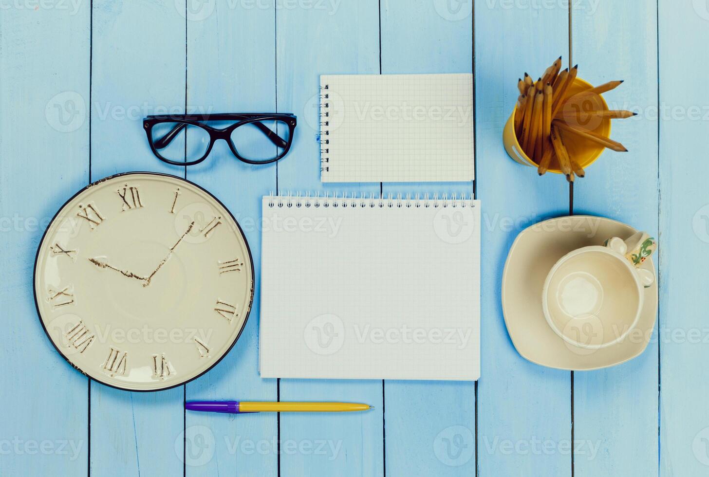 Workspace setup with stationery, a clock, and coffee on a blue wooden table captured in mid-morning light photo