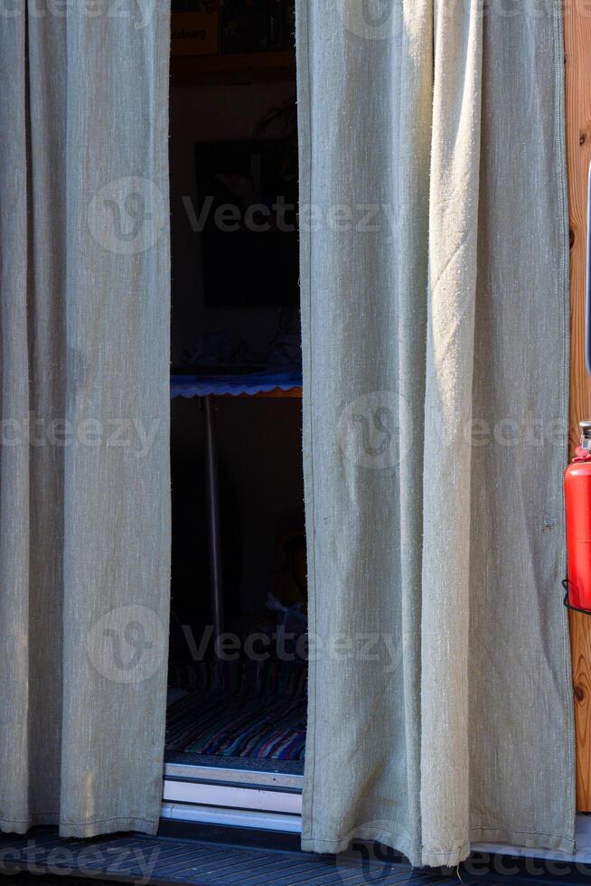 beige fabric curtains partially covering a camper van entrance, offering privacy and revealing a compact and minimalist living space, representing van life, travel, and alternative lifestyles. photo