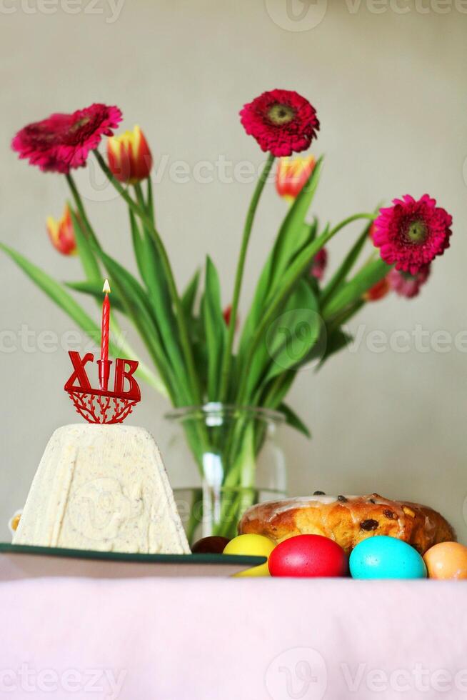 Orthodox easter table setting with colorful eggs, traditional cake paska bread, kulich, cheese paskha, burning candle, fresh flowers, and festive decor 4 photo