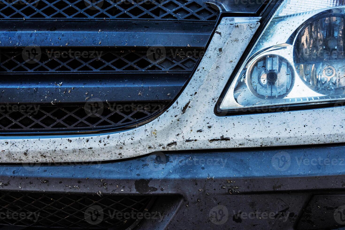Closeup of a dirty car front bumper, grille and headlight covered in insects and dirt after a long road trip. Dusty, bug splattered vehicle front end. photo