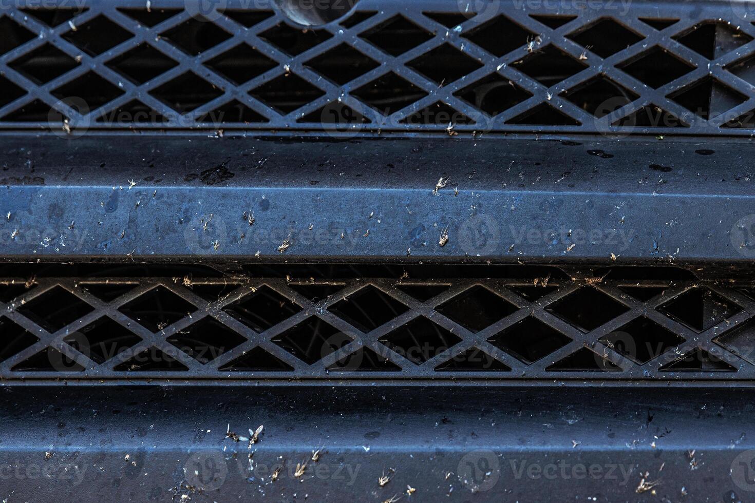 Closeup of a dirty bug splattered vehicle grille with dust and debris. Car front end bumper covered in insects and dirt after a long trip. Auto care, road conditions, air intake system photo