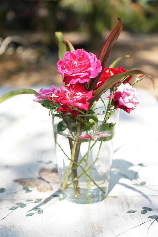 Pink and Red Roses in a Glass Vase on White Floral Pattern Table photo