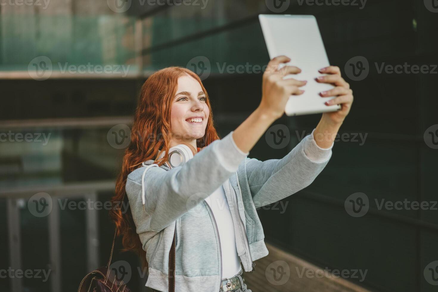 A Young Woman Delightfully Taking a Selfie with a Tablet in a Modern Urban Setting Around photo