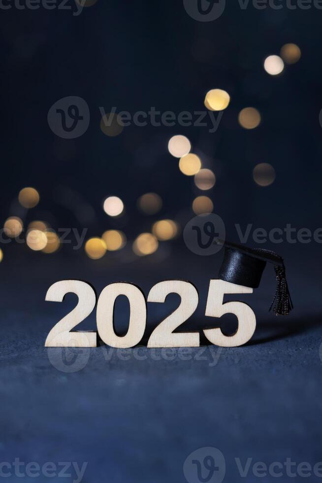 Graduation cap on wooden number 2025 on dark background with bokeh. Class of 2025 concept. photo
