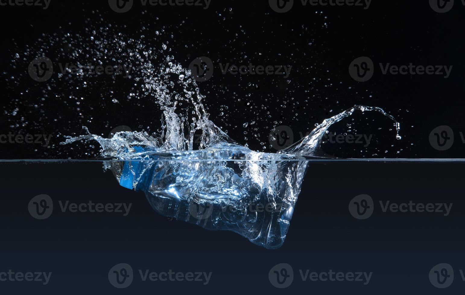 Front view of clear plastic bottle submerged in water causing a splash against black background photo