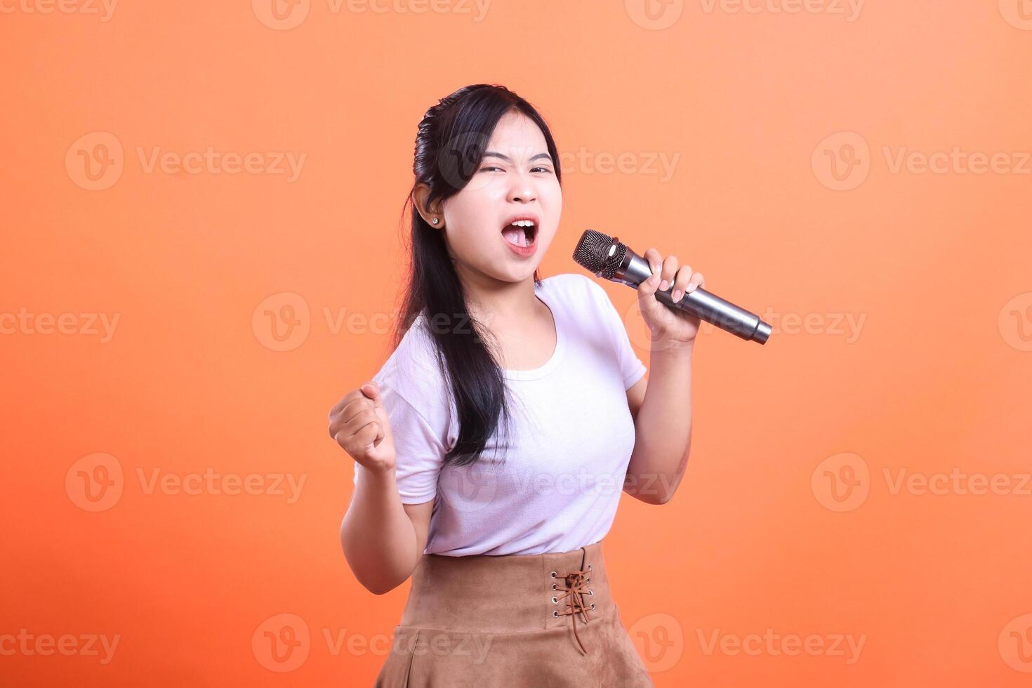 A young woman sings with passion, holding a microphone and demonstrating full emotion, with a vibrant and energetic presence. isolated on orange background photo