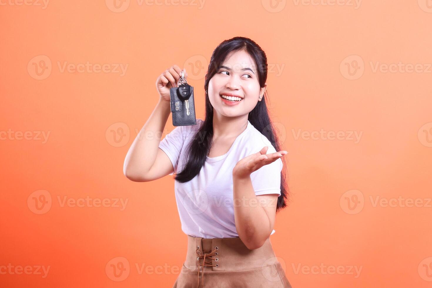 Excited Asian woman showing off her new car keys with a big smile. Looking to the side and presenting. isolated on orange background photo