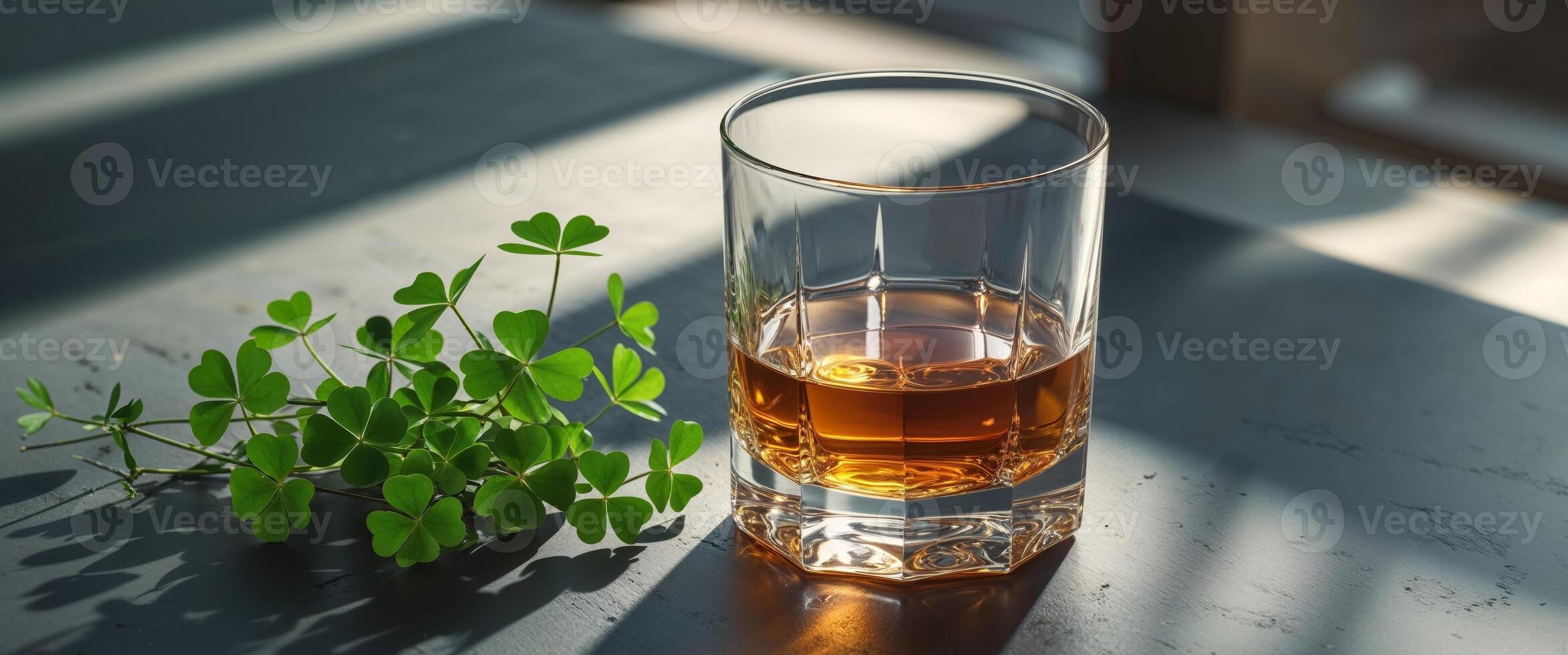 Golden whiskey in a glass next to fresh green clovers on a dark surface. photo