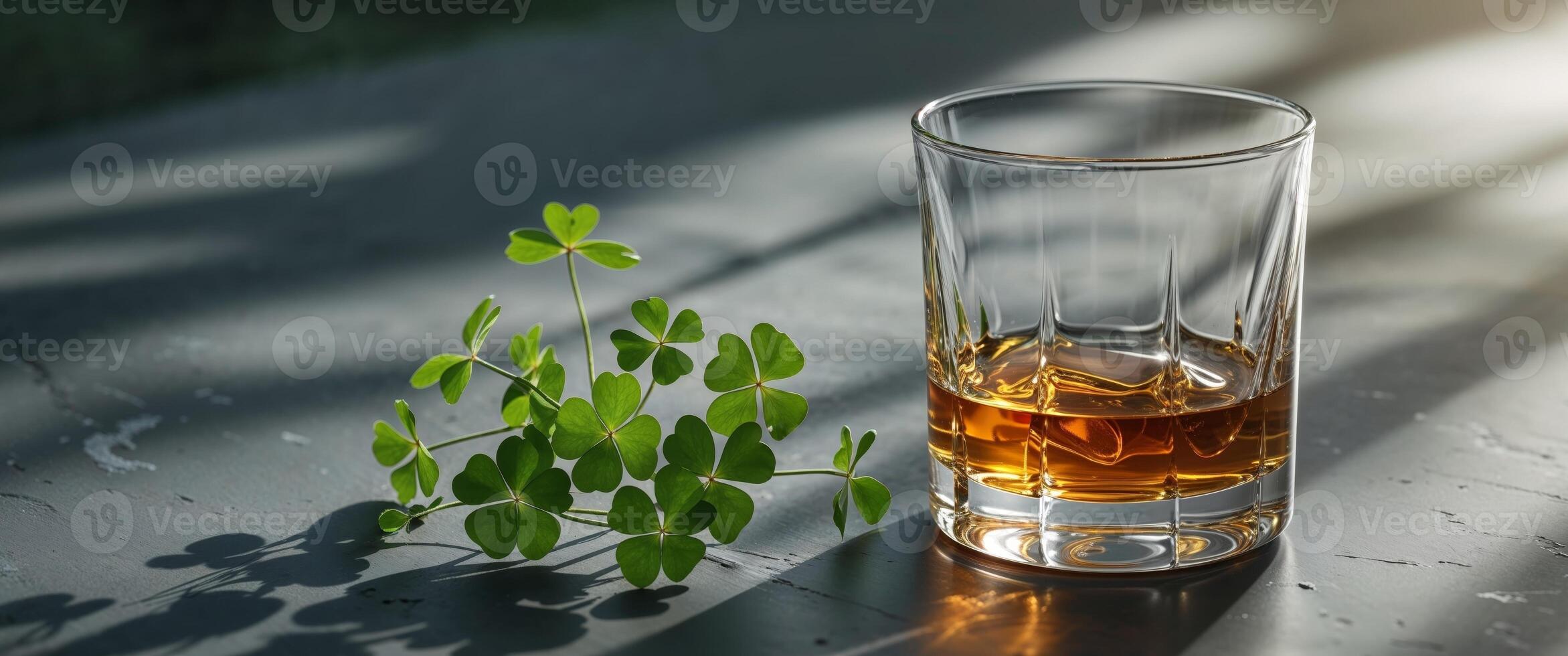 Golden whiskey in a glass next to fresh green clovers on a dark surface photo
