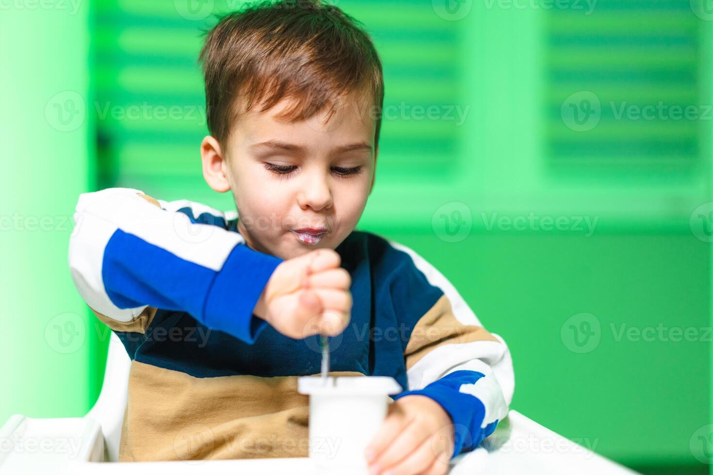 Boy enjoys sensory play. A child stirs a container with a spoon, exploring textures in a vibrant green environment. photo