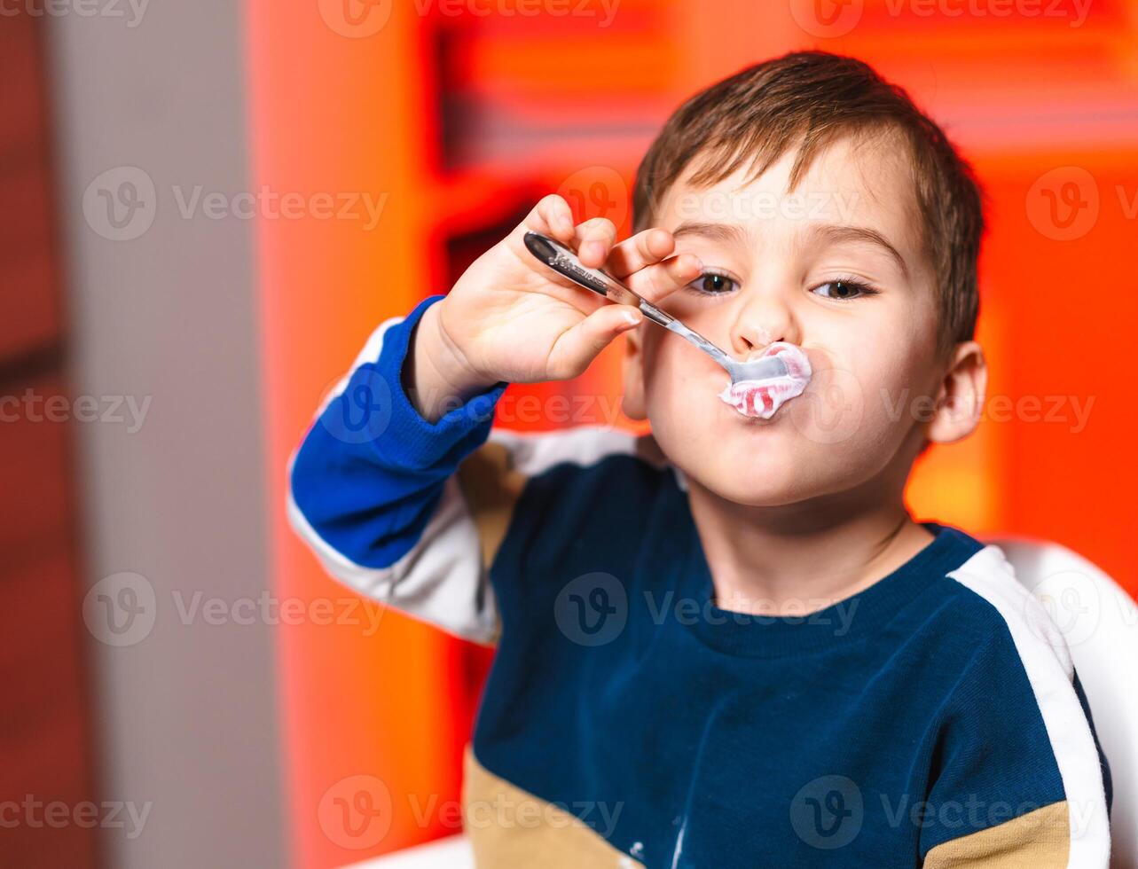 Child enjoying dessert with a spoon. A young boy smiles while playfully holding a spoon with dessert in his mouth, highlighting his joy. photo