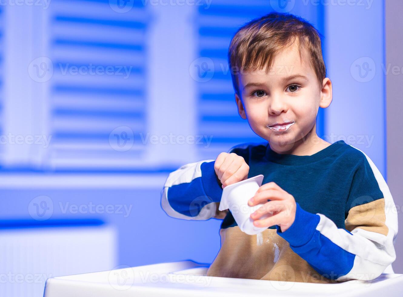 Child happily enjoying a treat. A young boy is happily eating from a cup, showcasing joy in a bright and colorful environment. photo