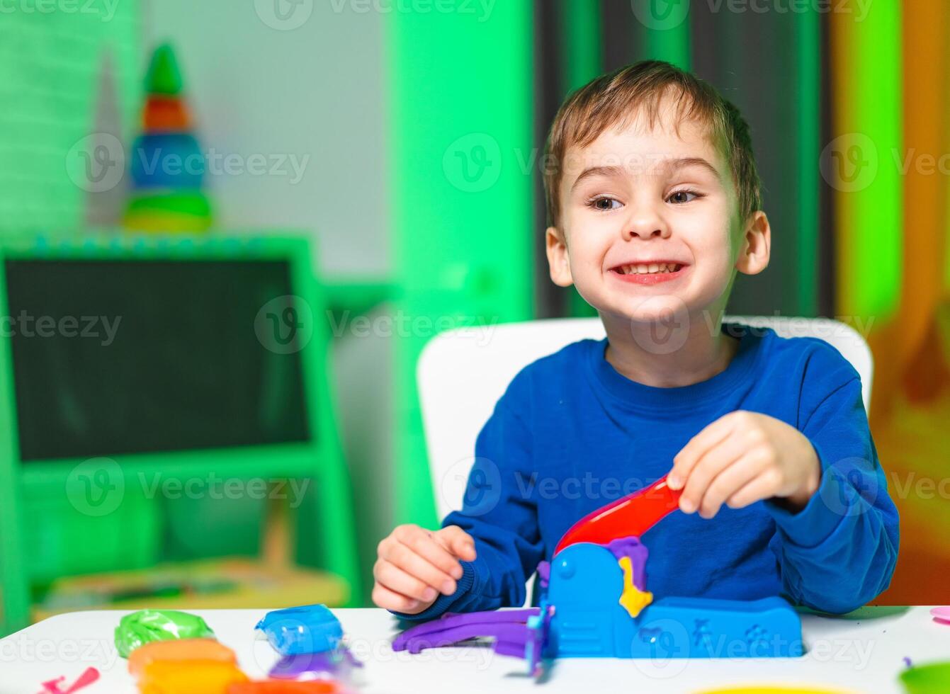 Child playing with colorful toys. A young boy smiles brightly while playing with vibrant toys at a table, showcasing joy and creativity. photo