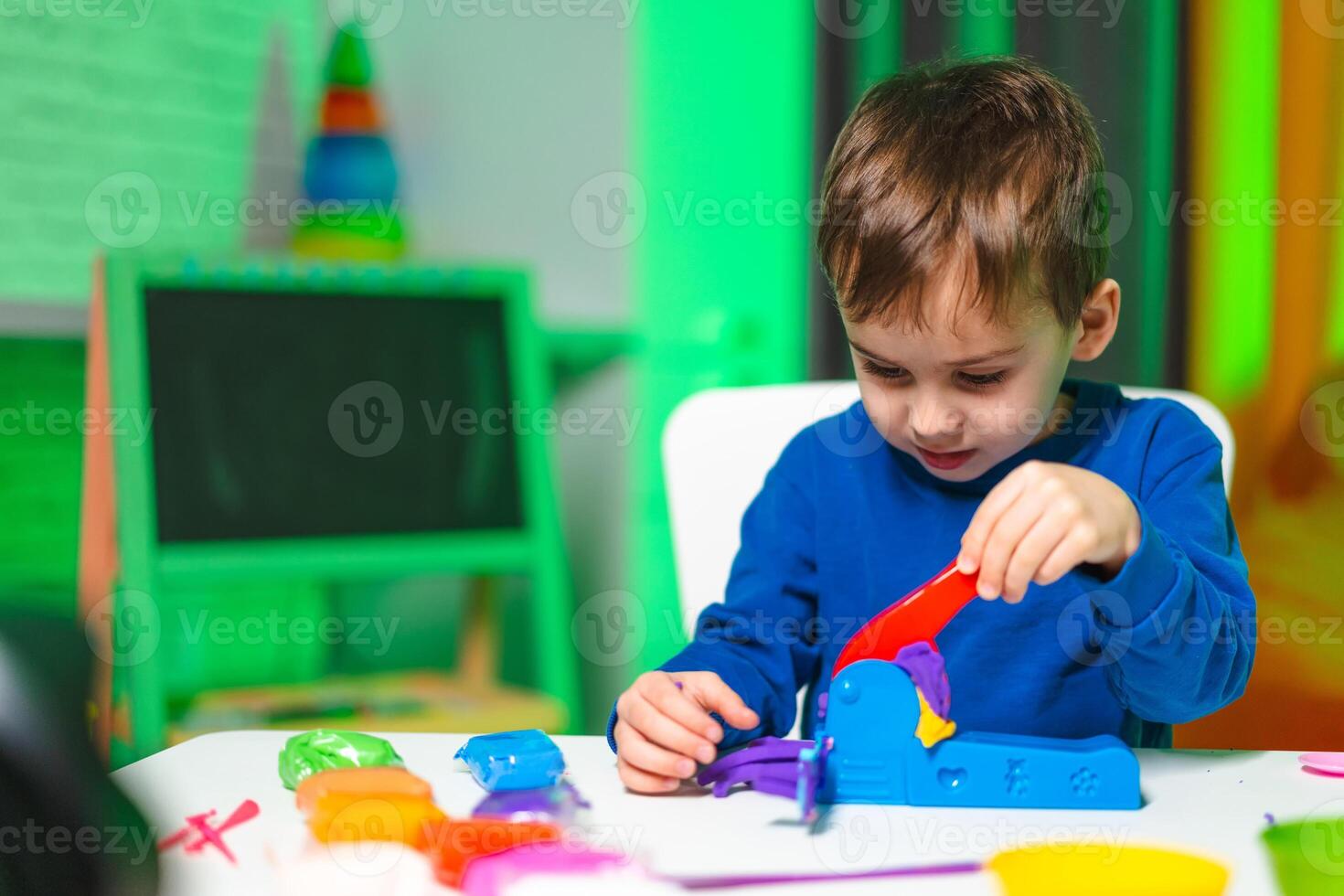 Kid molds bright clay shapes. Young boy enjoys creative activity with bright modeling clay at a brightly lit table filled with tools and clay shapes. photo