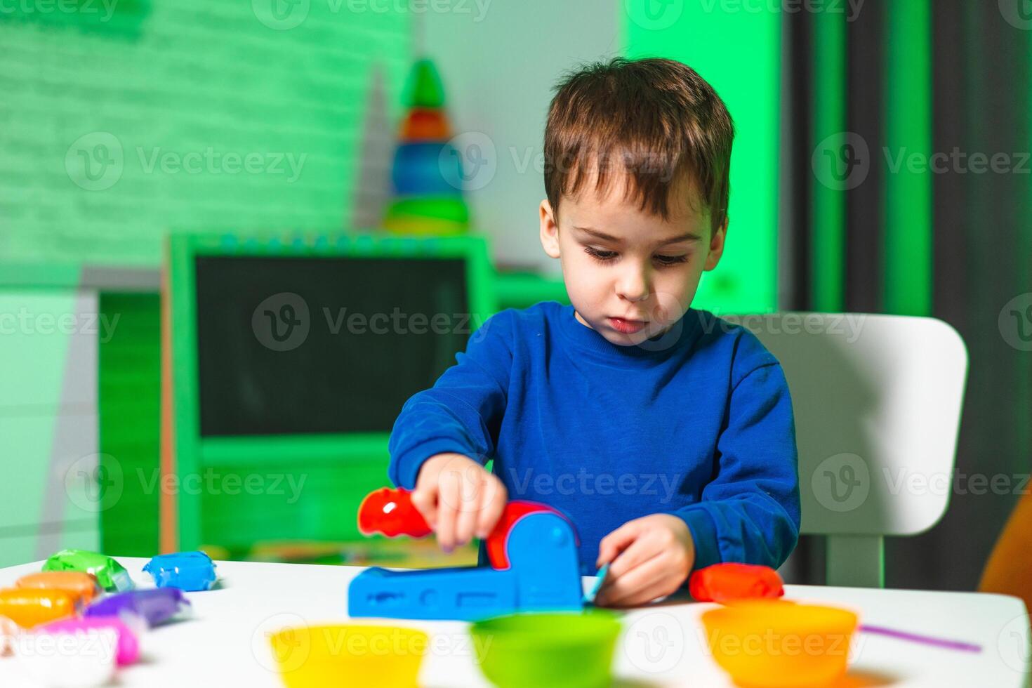 Child playing at a bright table. A young boy engages in playful activity with colorful toy tools and materials in a bright, cheerful room. photo