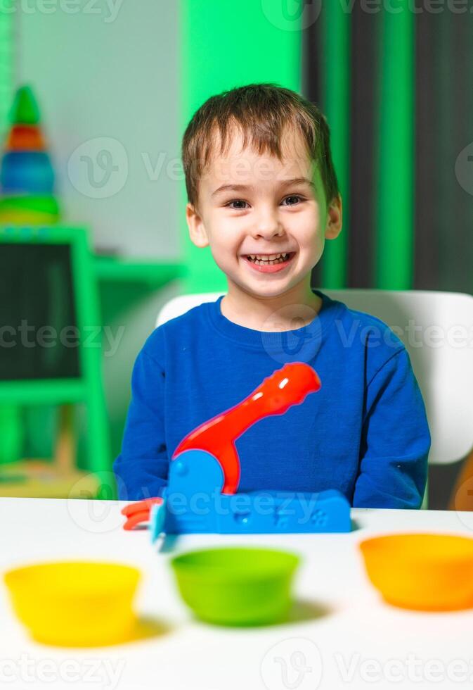 Boy plays with colorful toys. A young boy smiles while playing with bright plastic toys on a table in a vibrant playroom. photo