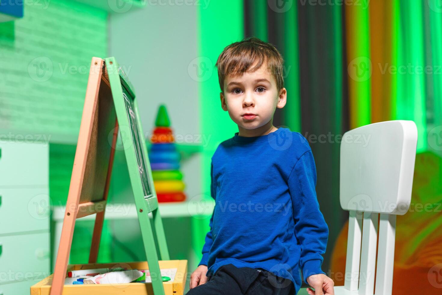 Young boy enjoys creative time at home. A boy at a green easel in a colorful room works on his art, surrounded by fun decor. photo