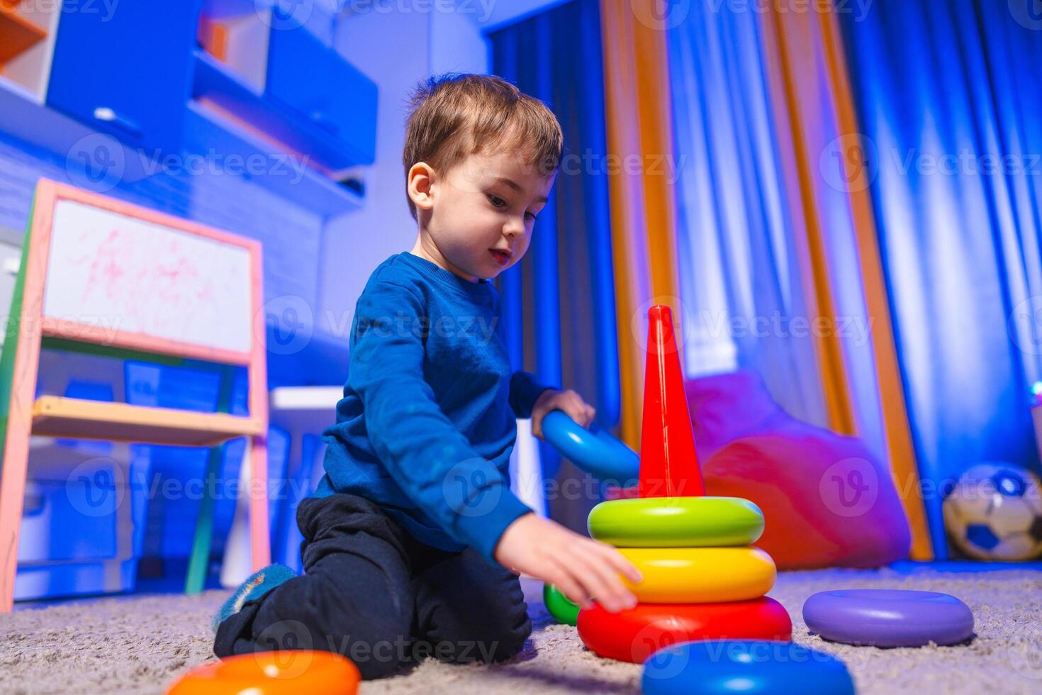 Child stacking colorful blocks. A young boy is playing with colorful stacking rings in a bright, playful room filled with toys and soft furnishings. photo