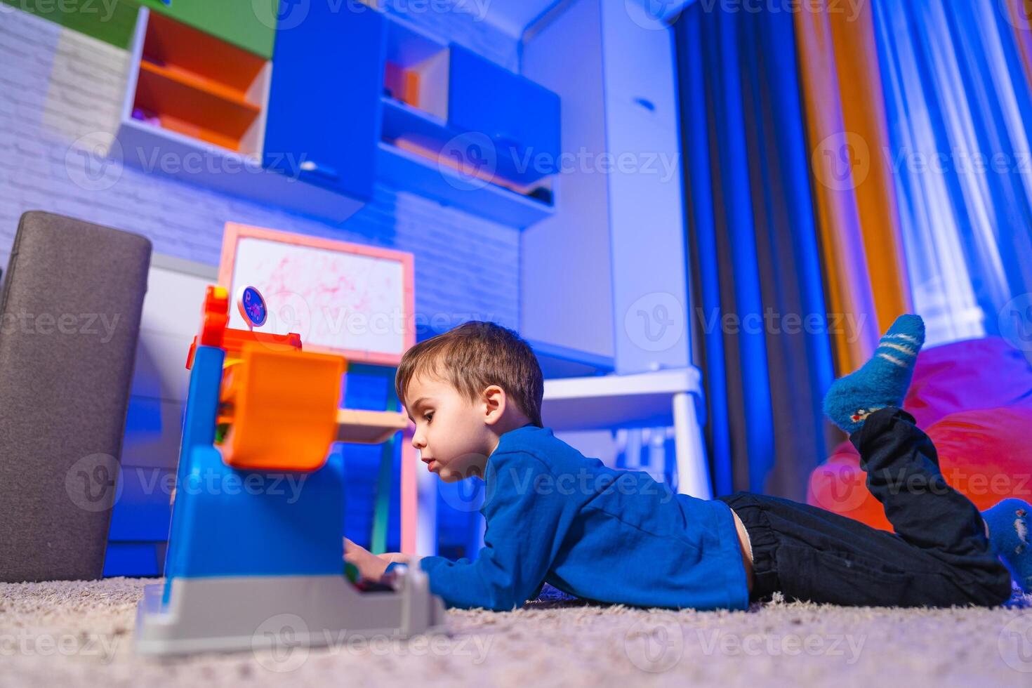 Boy playing with toy in living room. A young boy lies on the carpet, focused on a colorful toy in a bright living room with playful decor. photo