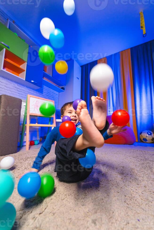 Child enjoys colorful ball play indoors. A joyful child plays with colorful balls in a bright indoor space while relaxing on a soft carpet. photo