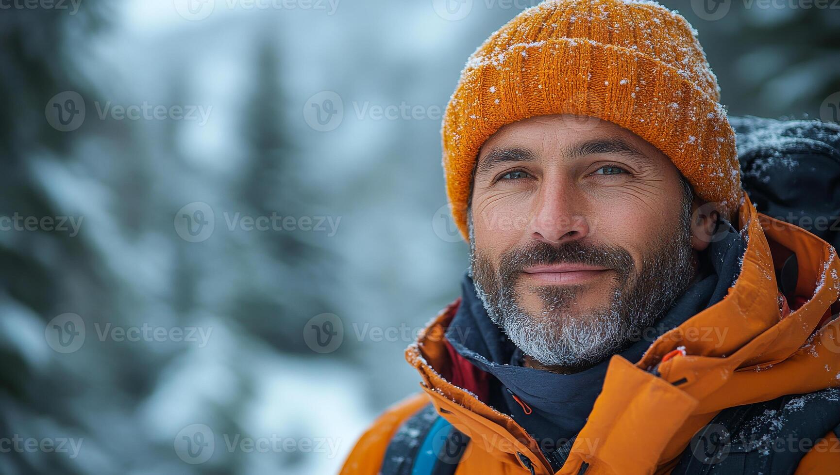 A man wearing a yellow hat and orange jacket is smiling. He is wearing a backpack and he is enjoying the outdoors photo