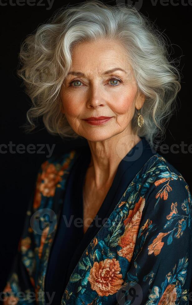 A woman with gray hair is wearing a floral print dress. She is smiling and looking at the camera photo