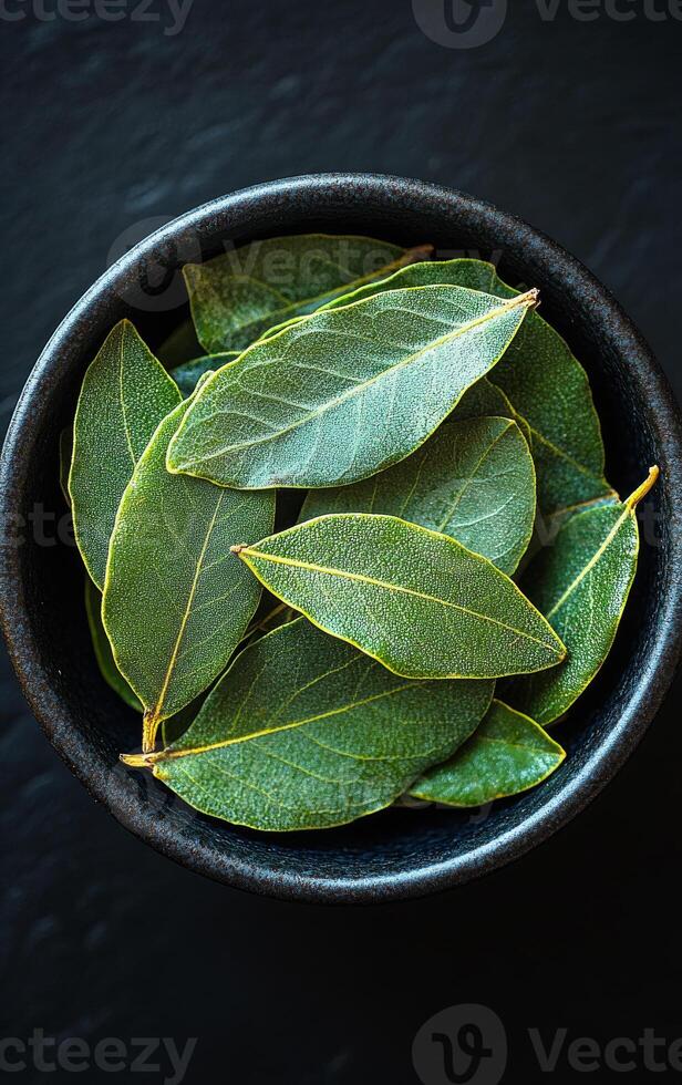 Fresh bay leaves in a bowl. A dark bowl filled with vibrant green bay leaves, ready for culinary use in various dishes and recipes. photo