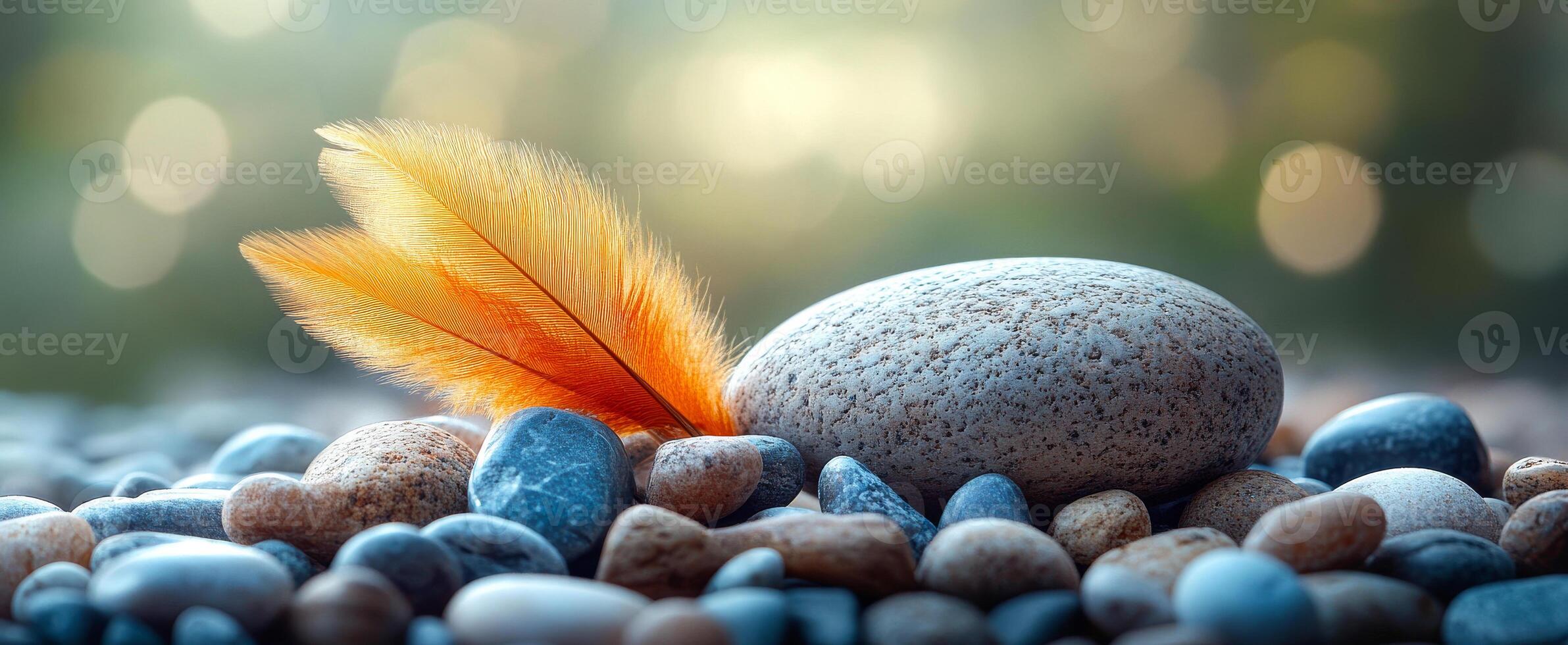 Orange feather on smooth stones. A vibrant orange feather is gently placed on a smooth grey stone among various pebbles. The background is blurred. photo