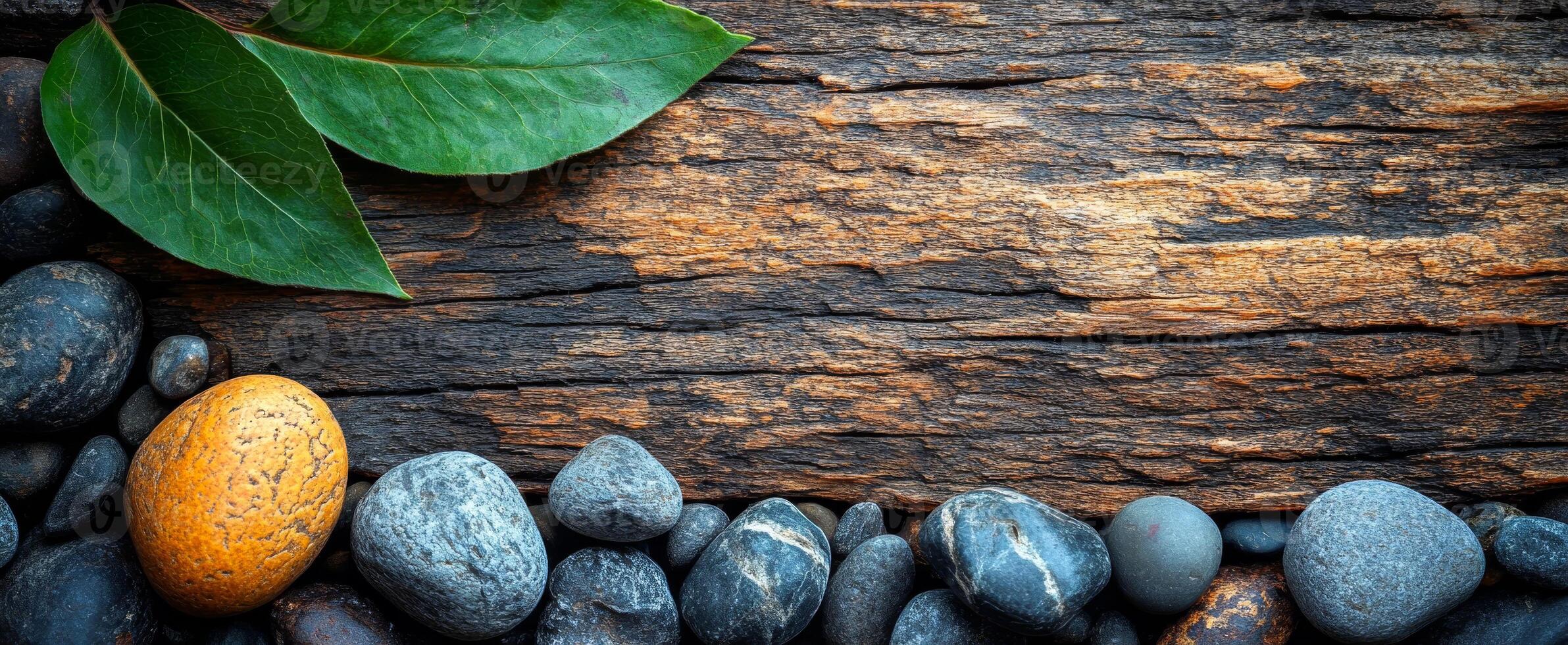 Stones and wood for tranquility. Smooth stones lie beside a weathered wood surface, contrasted by vibrant green leaves. photo