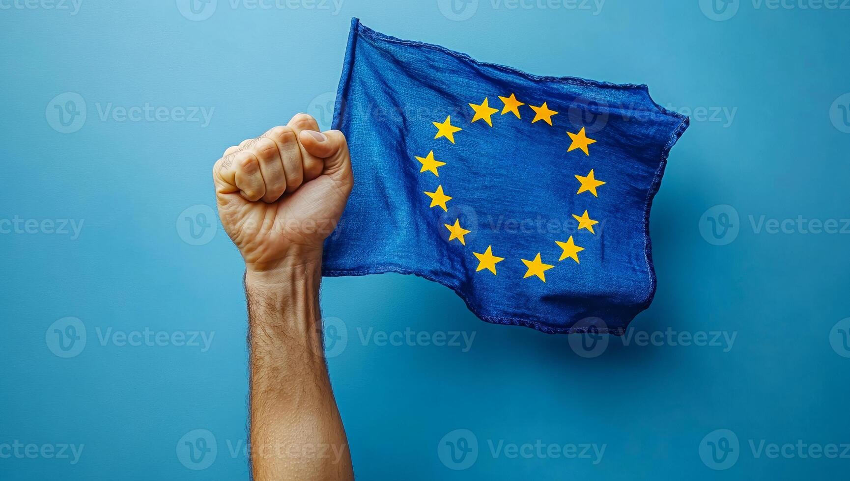EU flag raised in support. A hand holding the European Union flag high against a blue background, symbolizing unity and pride for the EU. photo