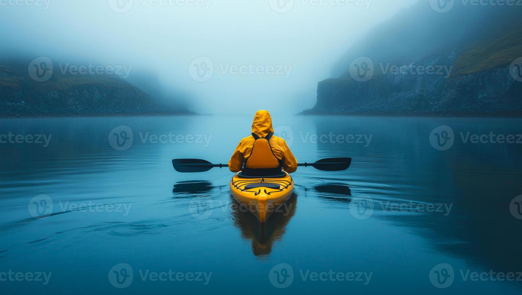 Yellow kayak in misty waters. A person in a yellow kayak paddles through calm, fog-covered waters surrounded by cliffs on a quiet morning. photo