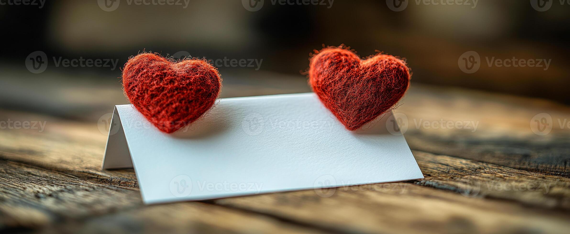 Two red hearts on a white card with a blank space. The card is on a wooden table photo