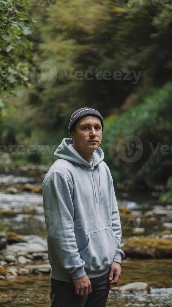 A man in a hoodie standing in front of a river photo