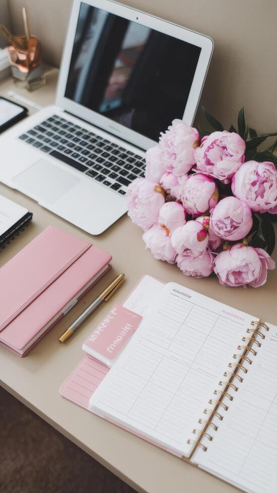 A pink notebook, pink flowers and a laptop on a desk photo