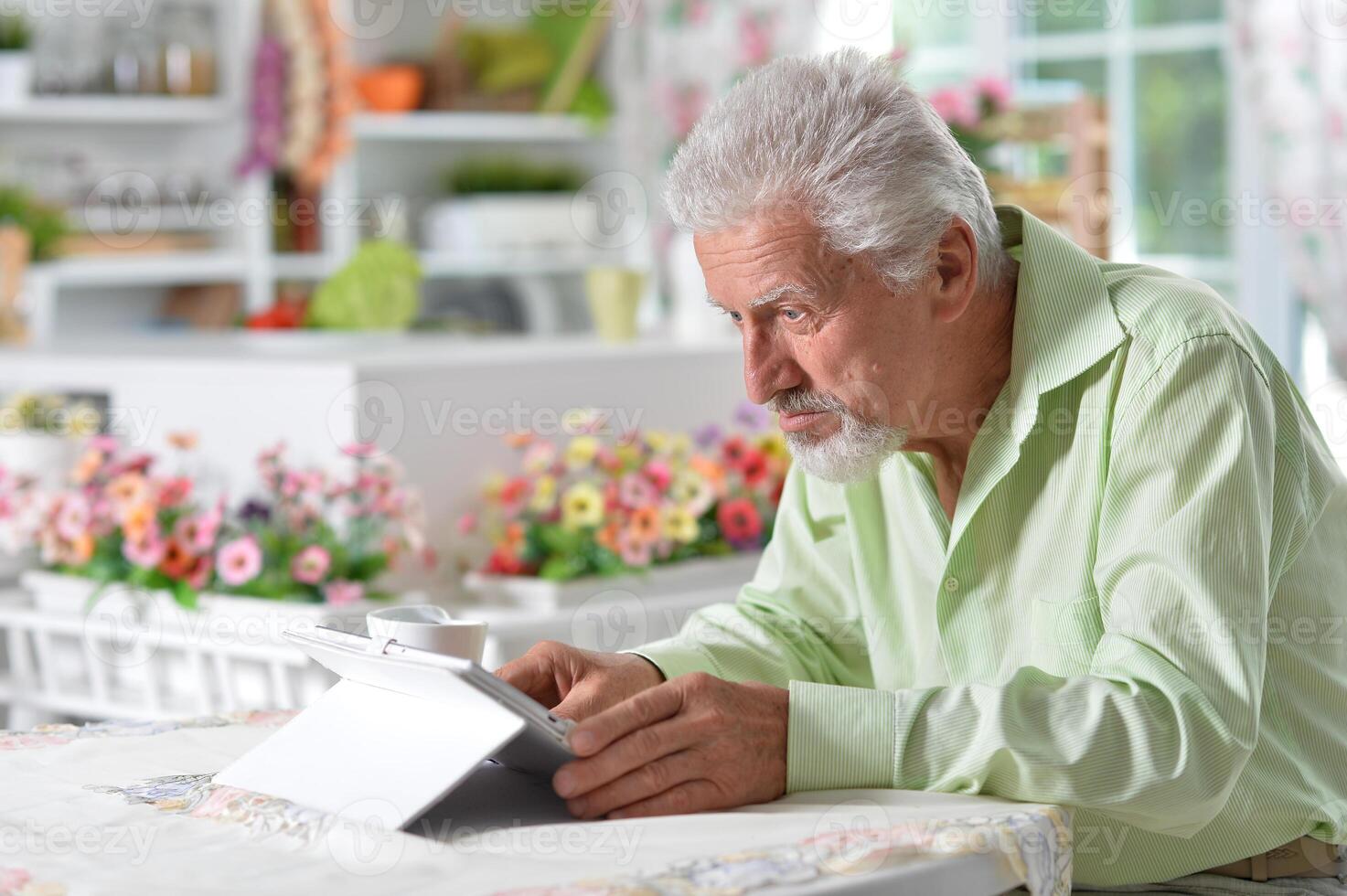 Elderly man posing at a table with a tablet photo