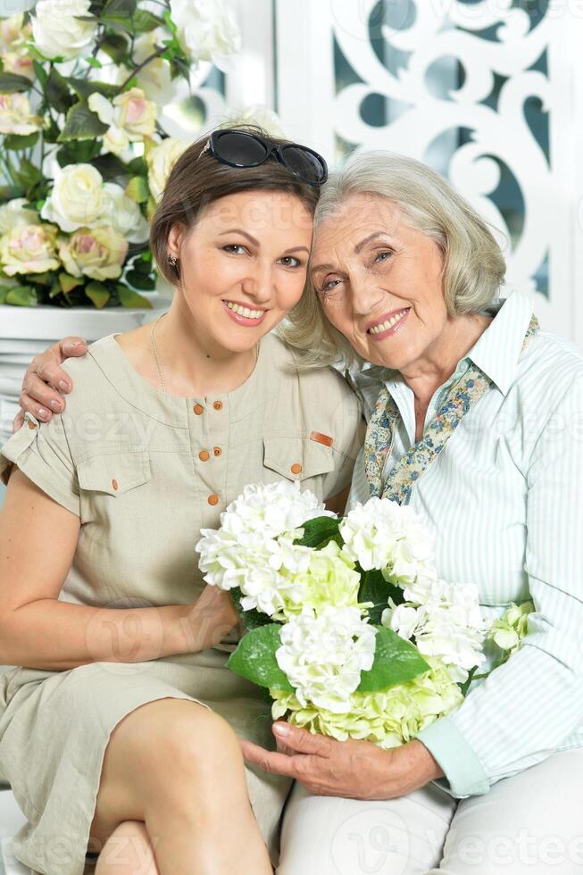 Elderly mother and daughter sitting on a bench surrounded by flowers photo