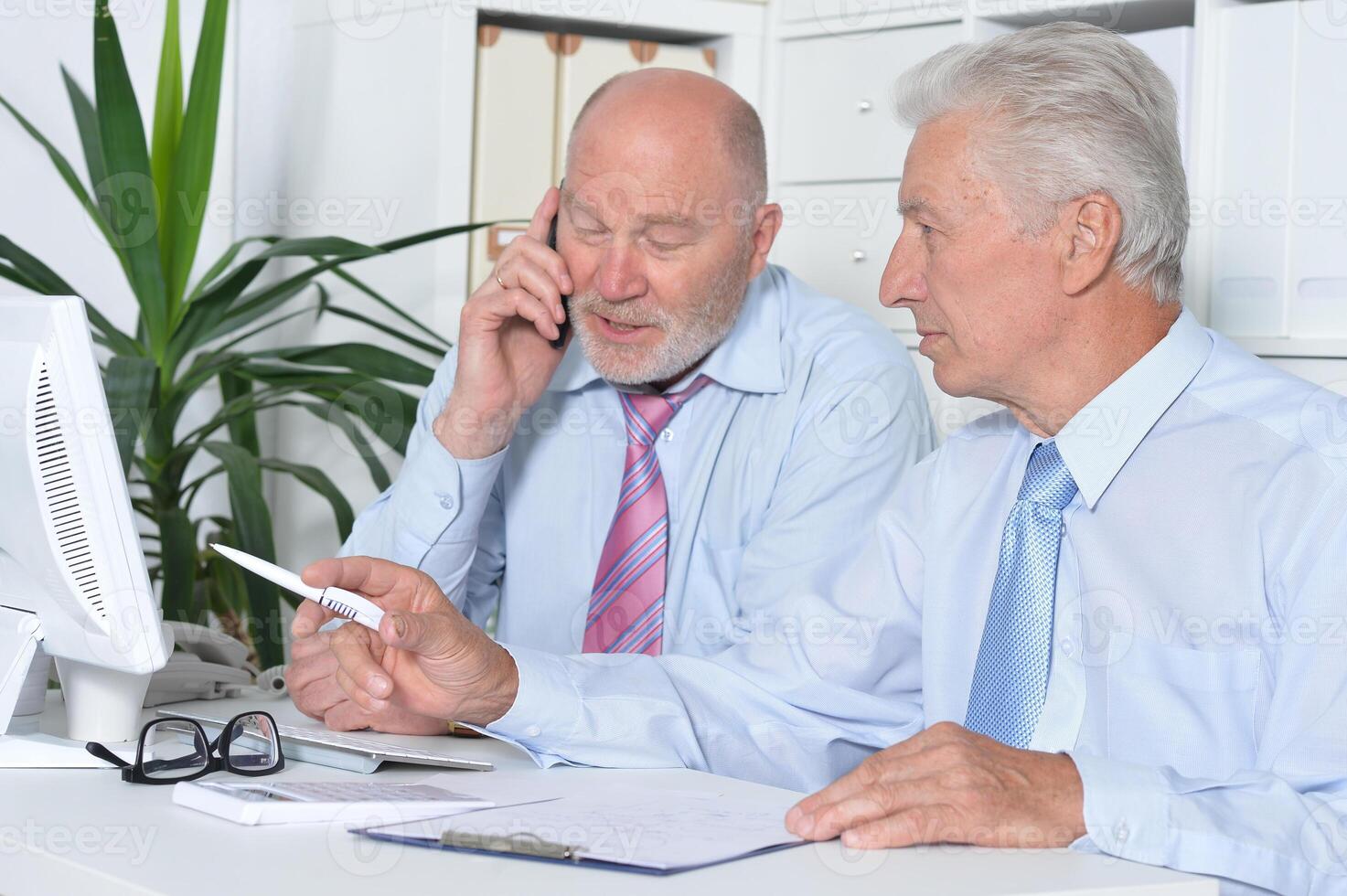 Two old business men sitting at desk and working photo