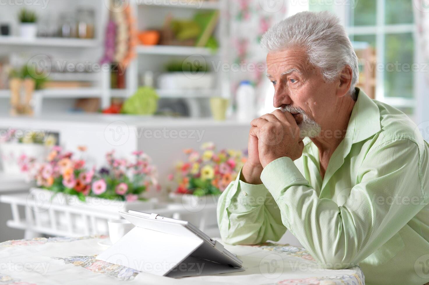 Elderly man posing at a table with a tablet photo