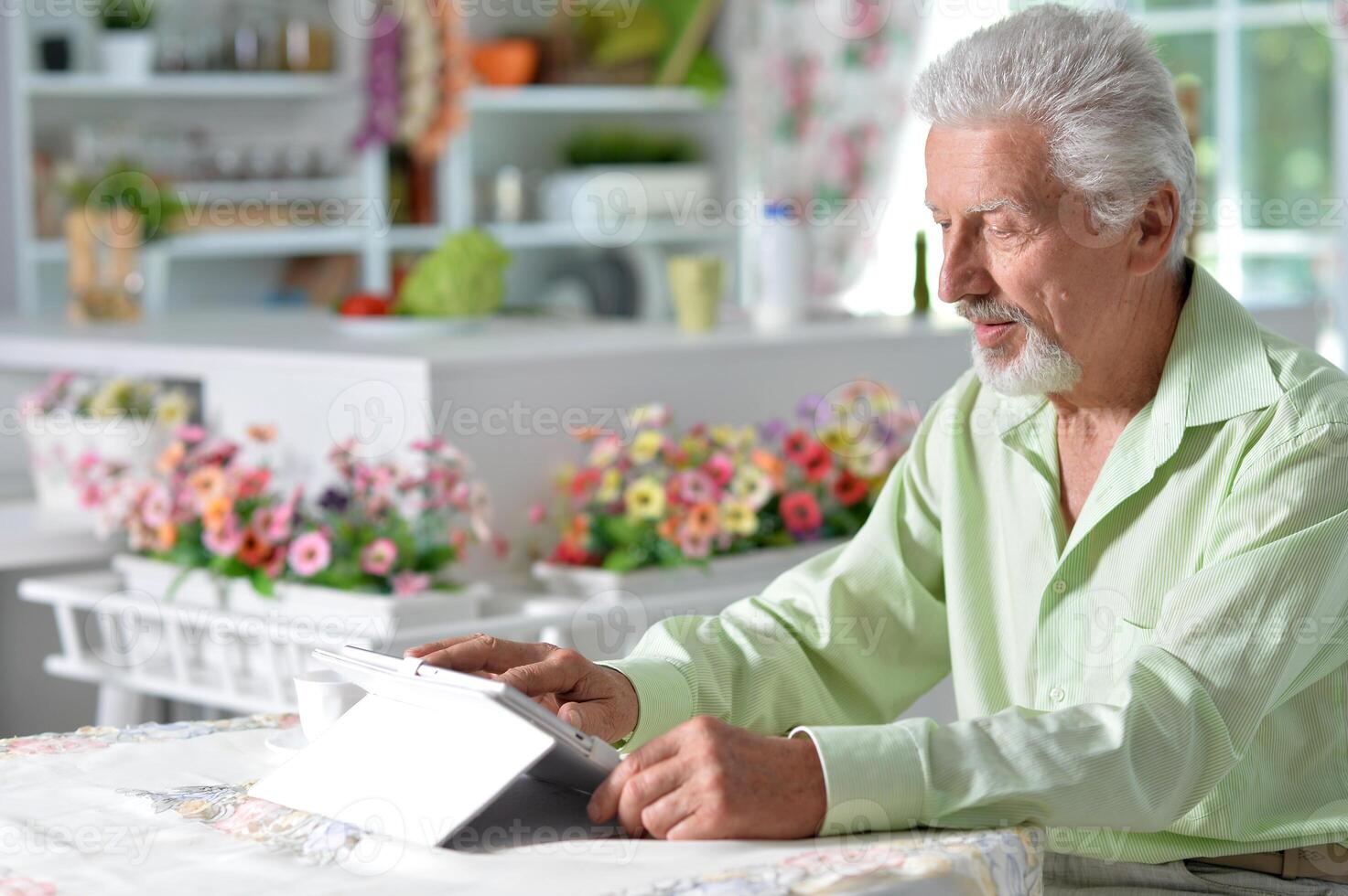 Elderly man posing at a table with a tablet photo