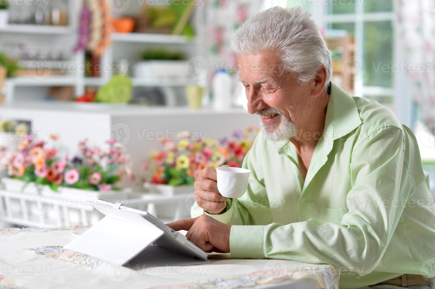 Elderly man posing at a table with a tablet photo