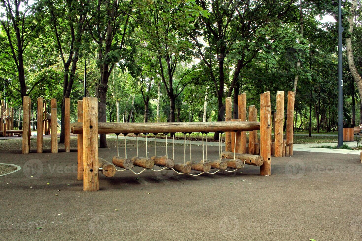Wooden playground climbing frame with rope ladder and slide in a green park. Sunny day with trees in the background. Children's outdoor activity and recreation photo
