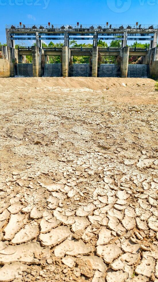 Arid Landscape with Cracked Earth and Dam Structure Under Clear Blue Sky Highlighting Water Scarcity and Environmental Challenges photo