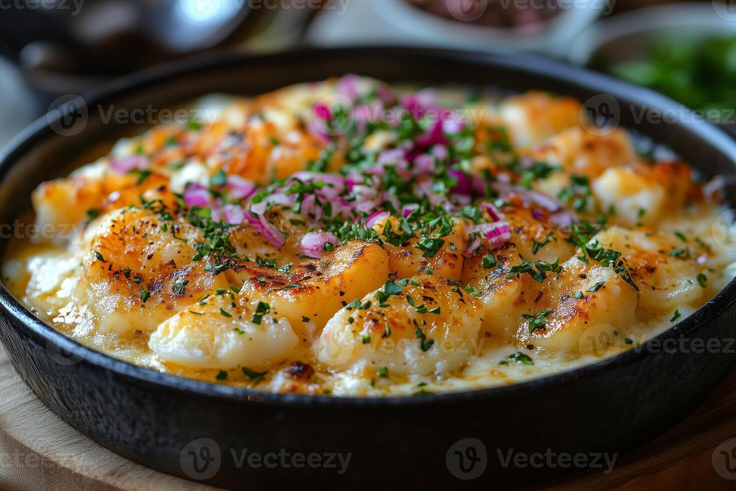 Scallops au gratin with bechamel sauce, parsley and red onion, served in a cast iron pan photo