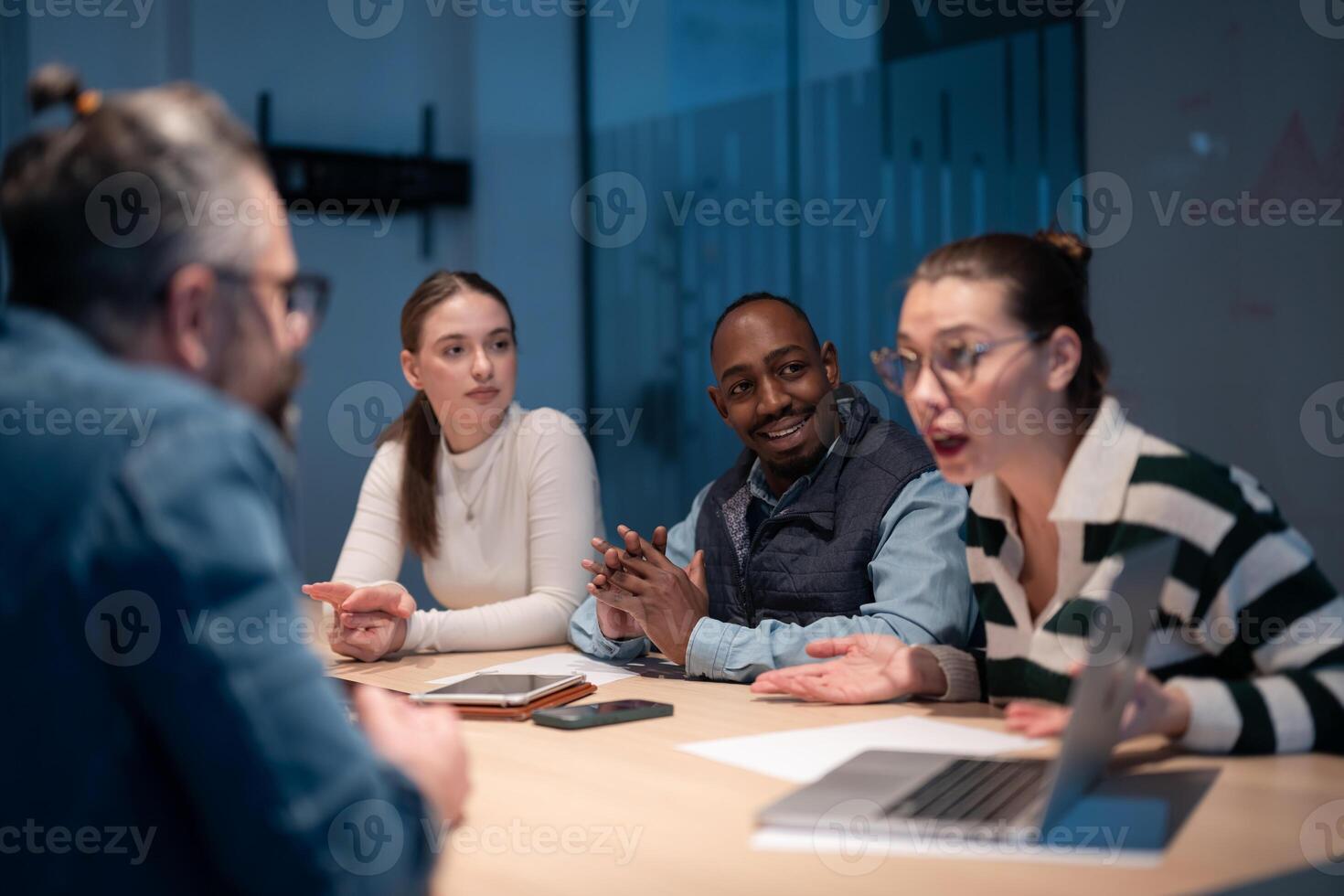 A diverse team of young professionals collaborates in a modern office conference room. Businesspeople discuss strategy, technology, and planning, using laptops to develop an innovative e-commerce photo